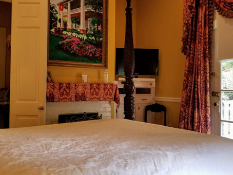 The historic Garden Guest Room at the Judge Porter House B&B featuring a large four-poster bed with elegant drapery, rich yellow walls, and classic antique furnishings.