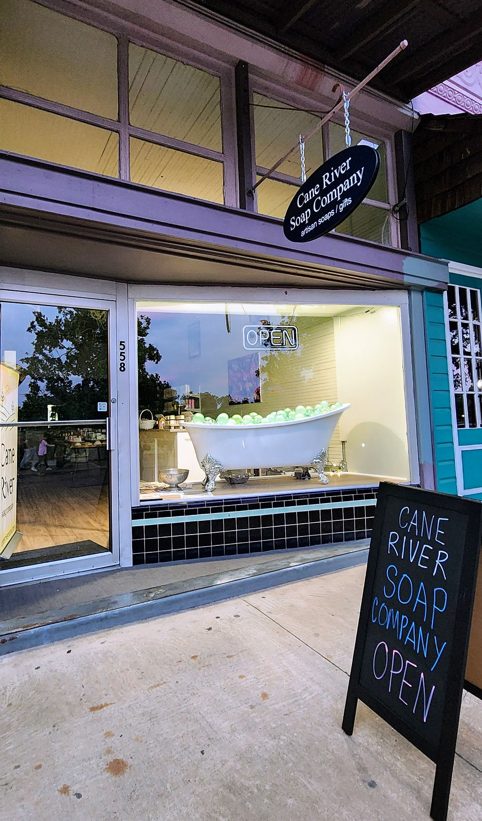 Cane River Soap Company storefront with a tub of green balls in the window, a chalkboard sign reads "OPEN", creating a welcoming vibe.