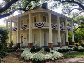 Two-story house adorned with red, white, and blue banners. Surrounded by greenery and trees. Sign reads, "Judge Porter House Bed & Breakfast."