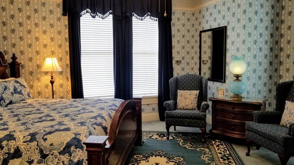 King sized bed and sitting area in the Blue Room with original stained glass window at Queen Anne B&B