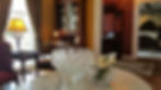 Crystal bowl and white roses on a marble table in an elegant room with vintage furniture, warm lighting, and a view into a bedroom.