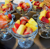 A serving tray holding elegant pedestal crystal bowls filled to the brim with freshly sliced strawberries, ripe pineapple chunks, and sweet red grapes for a gourmet breakfast.