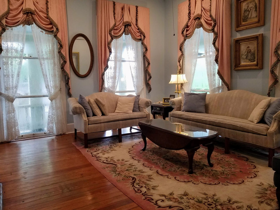 Elegant living room with beige sofas, pink drapes, lace curtains, ornate rug, and framed pictures. Warm, inviting atmosphere.