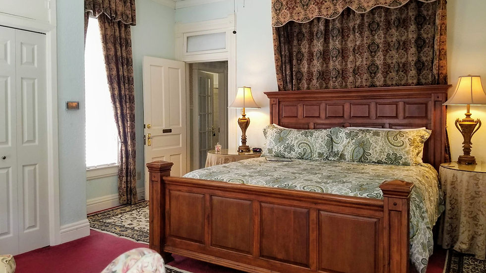 Elegant bedroom with a wooden bed, paisley bedding, and floral curtains. Two lamps on round tables illuminate the cozy setting.