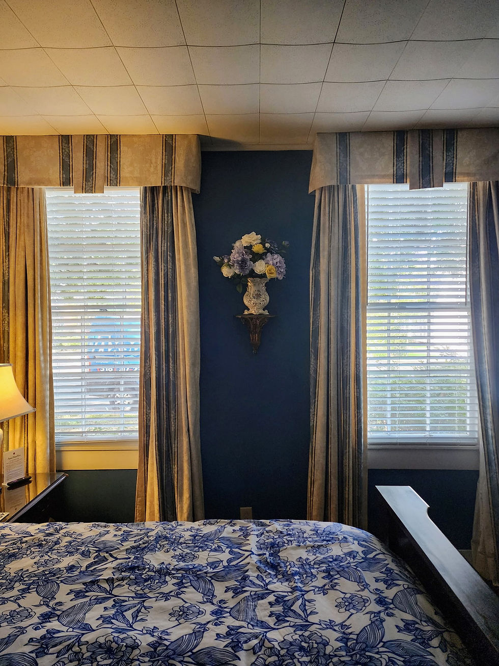 Spacious Ducournau Suite bedroom at Andrew Morris House featuring a vibrant floral arrangement on a wall shelf set between two large sunlit windows.