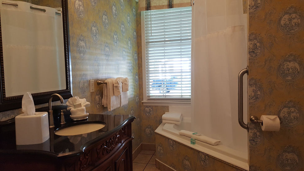Elegant bathroom with a decorative sink, floral wallpaper, towels on rack, and a bath with curtain. Sunlight filters through blinds.