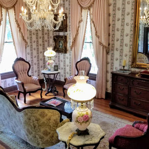 A stunning view of the Queen Anne B&B downstairs parlor with a crystal chandelier and antique Victorian furniture, highlighting the best rated bed and breakfast in Natchitoches.