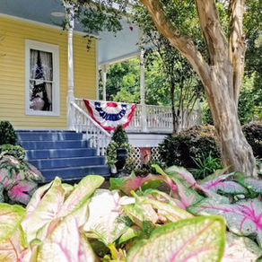 Queen Anne Bed and Breakfast in Natchitoches, Louisiana, surrounded by colorful gardens and its inviting side porch.