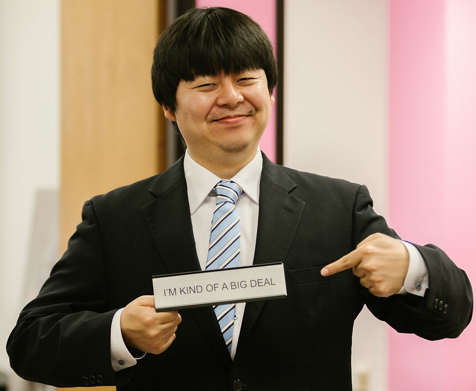 Asian man in a suit smiling and holding a sign that says, "I'm kind of a big deal."