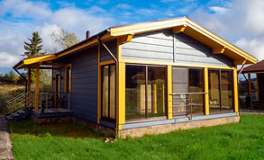 Cottage on a green lawn. House with a glazed terrace. House in a cottage village against a