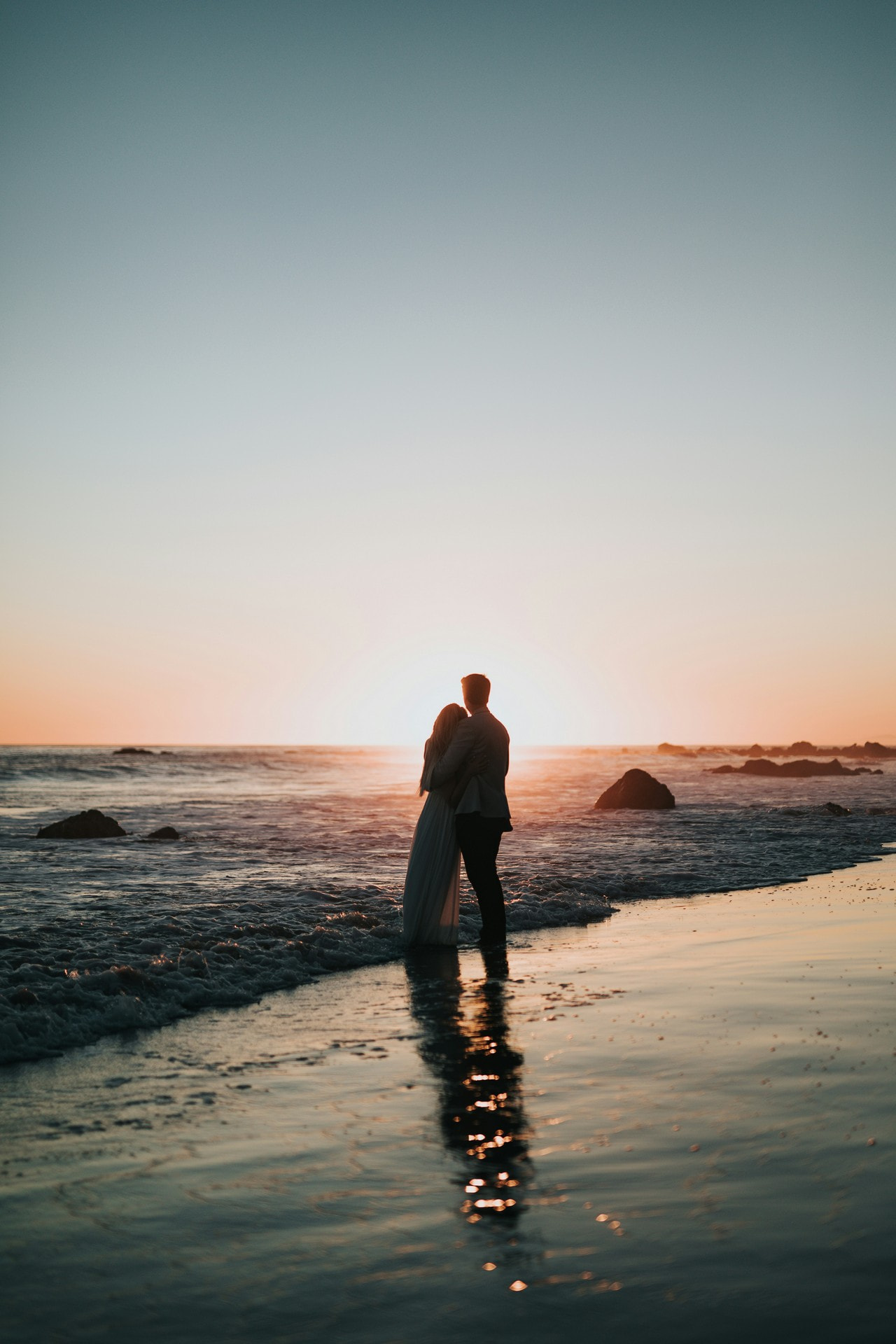 Couple heureux, soudés dans leurs projets d'enfant, regardant un coucher de soleil sur une plage
