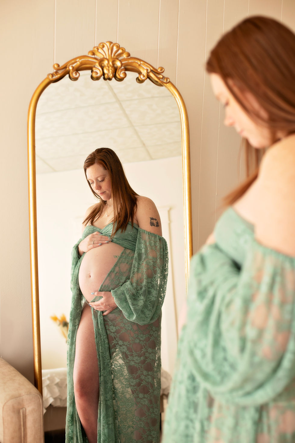 Pregnant woman in green lace robe, looking in mirror.