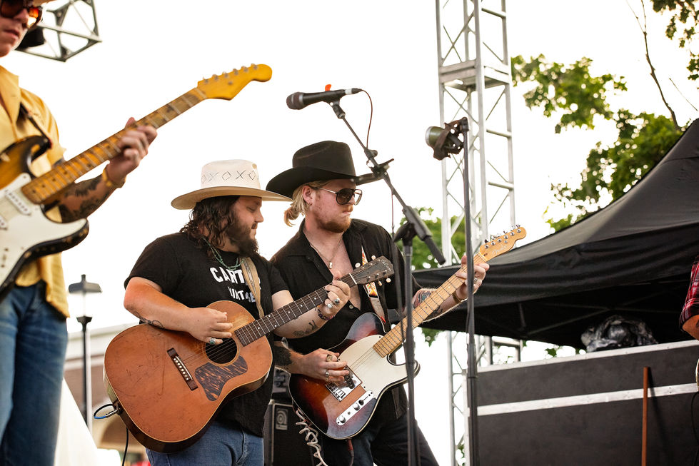 Three musicians playing guitars on an outdoor stage.