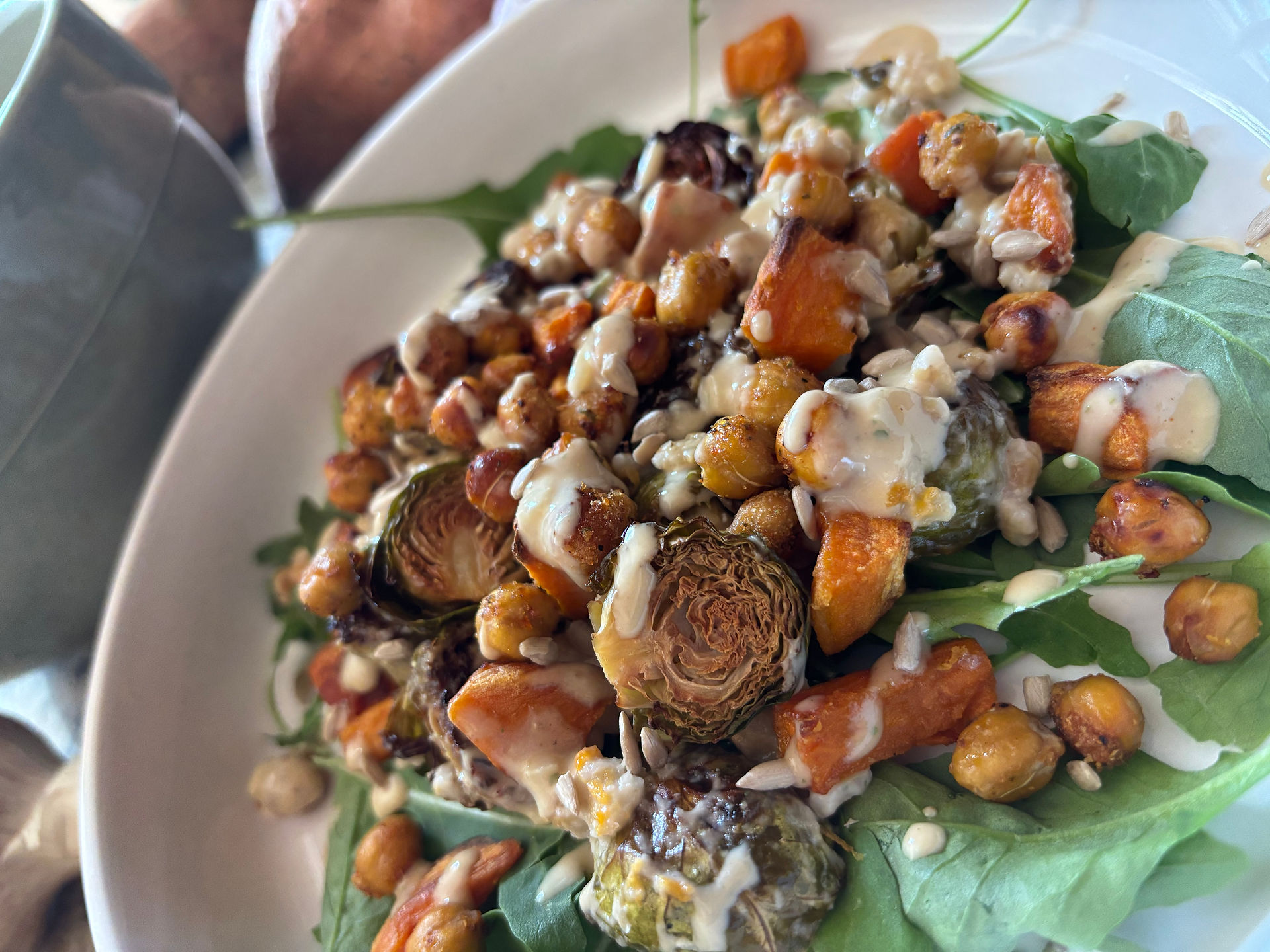 Roasted veggie salad with Brussels, sweet potato and chickpeas over a bed of arugula with tangy tahini vinaigrette and sunflower seeds 