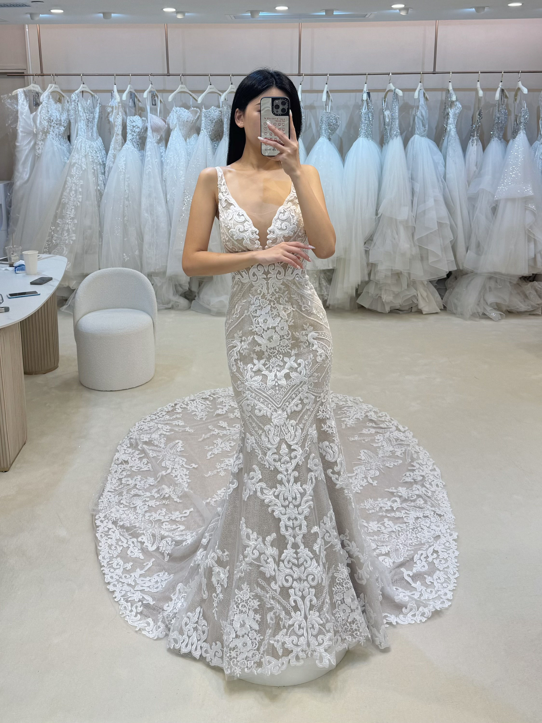 A bride-to-be wearing a mermaid-style wedding gown with a deep-V neckline and intricate white baroque lace over a champagne l