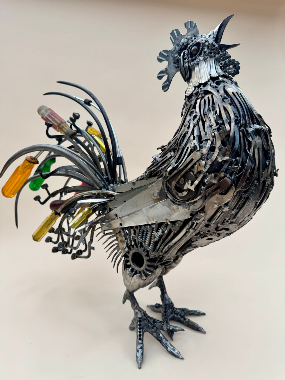 Front/Right side view of a crowing rooster with a colorful tail made primarily of screwdrivers and typewriter keys.