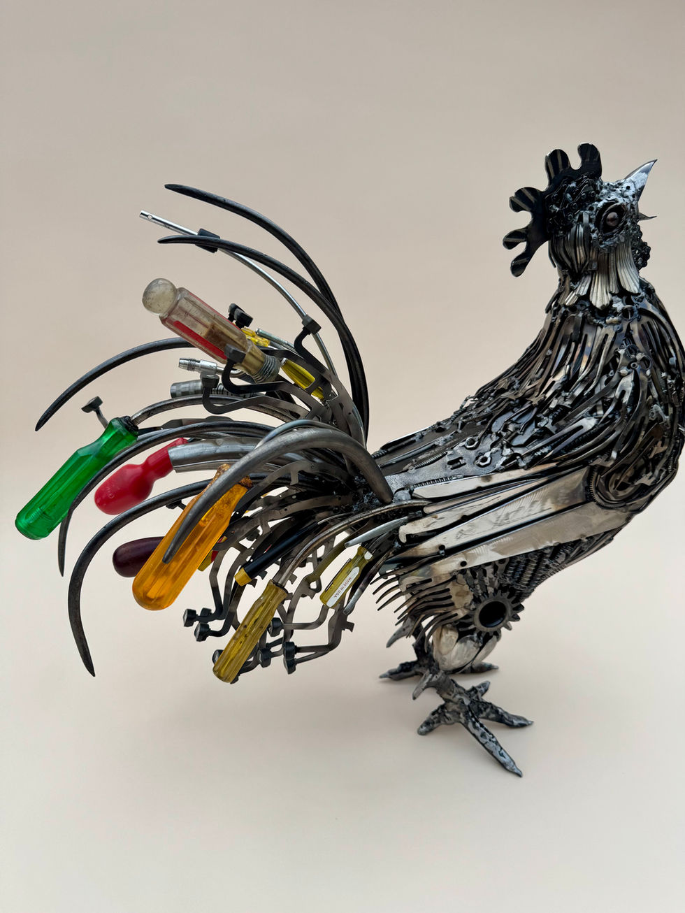 Right side view of a crowing rooster with a colorful tail made primarily of screwdrivers and typewriter keys.