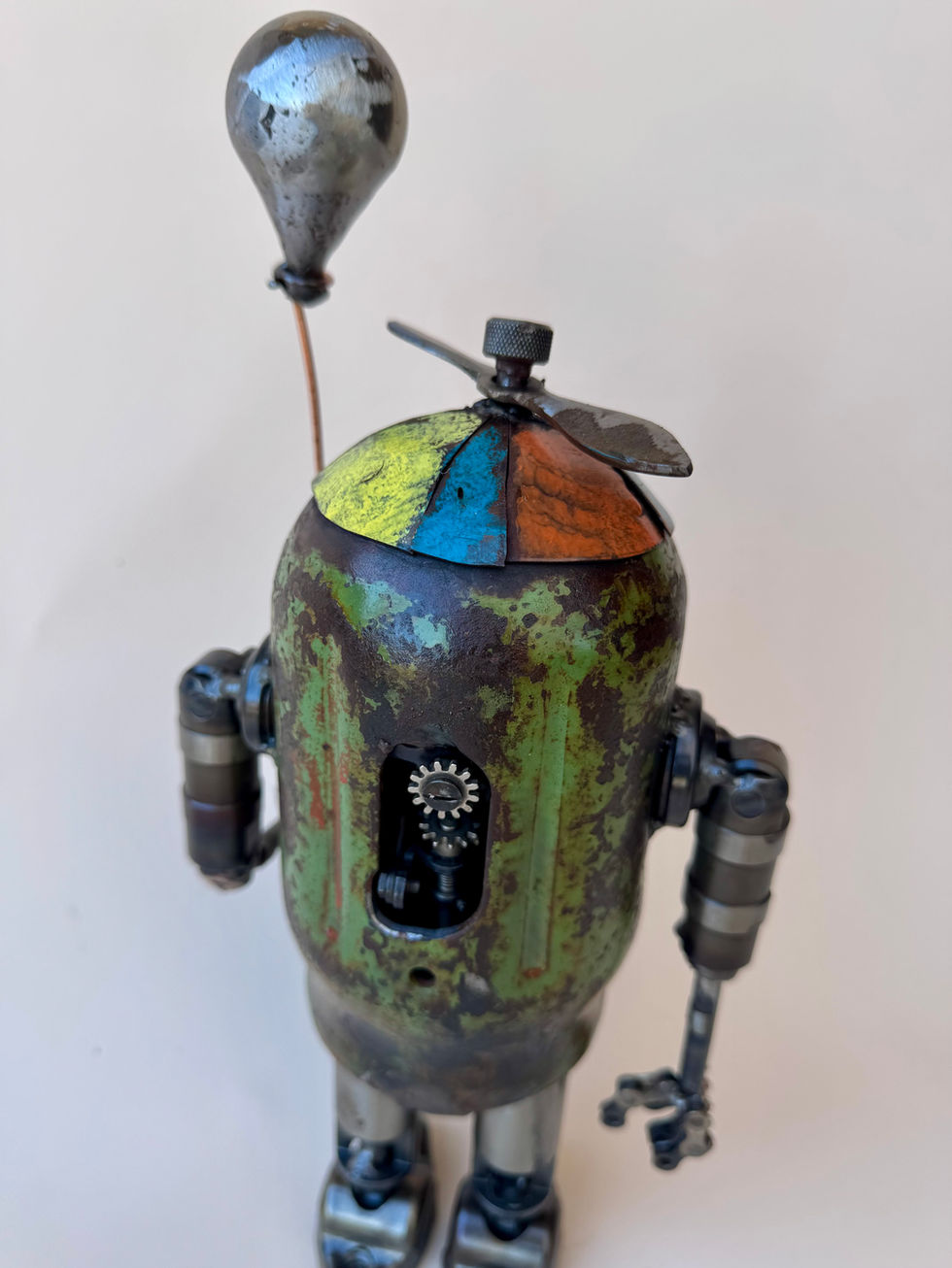 Rear view of a small, green, little boy robot holding a balloon. this view shows the inner workings of this "vintage" robot.