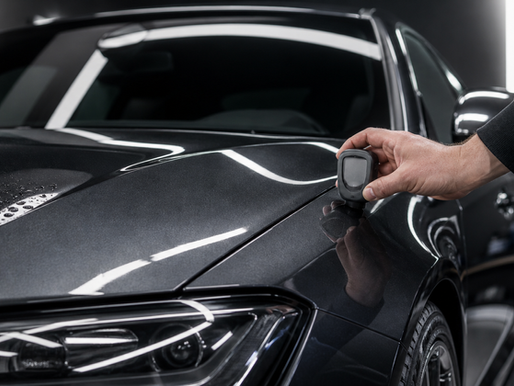 A detailer measuring the paint depth on a glossy new car in a professional studio