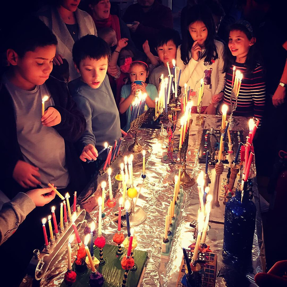 Families light menorahs at a Chanukah party with Amherst Neighborhood Captain, Lili