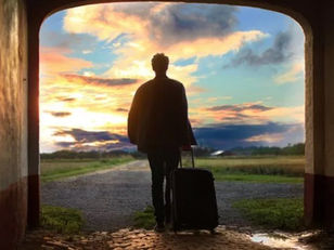 A person walking through a doorway with a suitcase toward a bright horizon, symbolizing the company’s ability to attract top talent through the candidate journey shaped by the hiring manager.