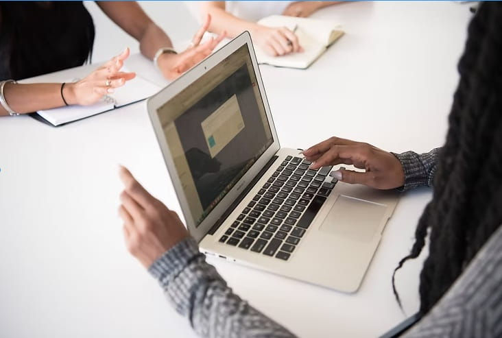 Women collaborating at a desk, one on a computer—Reservoir Modeling Expert case study in E&P software innovation.