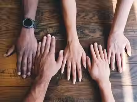 Top-down view of diverse hands resting on a shared table, representing workplace diversity and a culture of belonging across different backgrounds, genders, and identities.