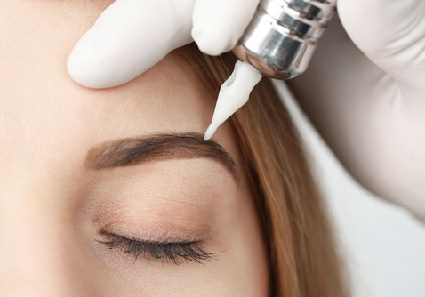 Eyebrow microblading procedure on a woman's face with a tattoo machine