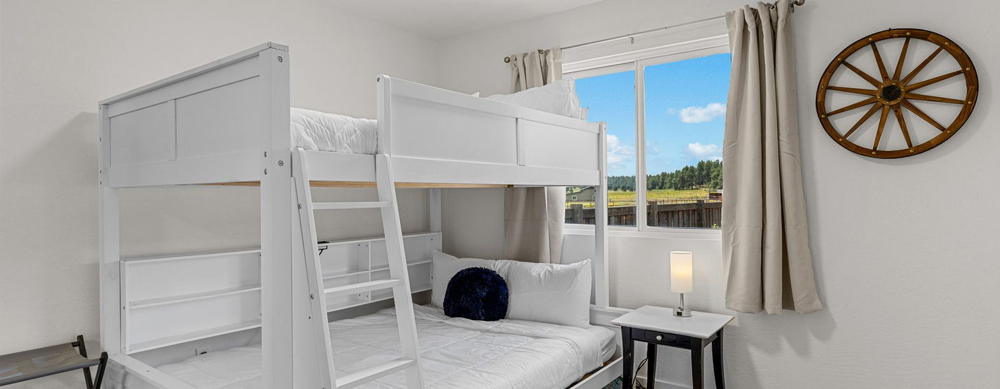 Bedroom with white queen-over-queen bunk beds and a window overlooking the meadow
