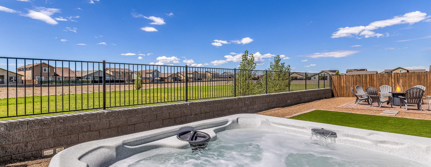 Bubbling hot tub in the backyard with open field views beyond the fence