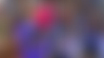 Children gather around a glowing fish tank and listen to a book reading in a library. Bookshelves line the walls, creating a cozy atmosphere.