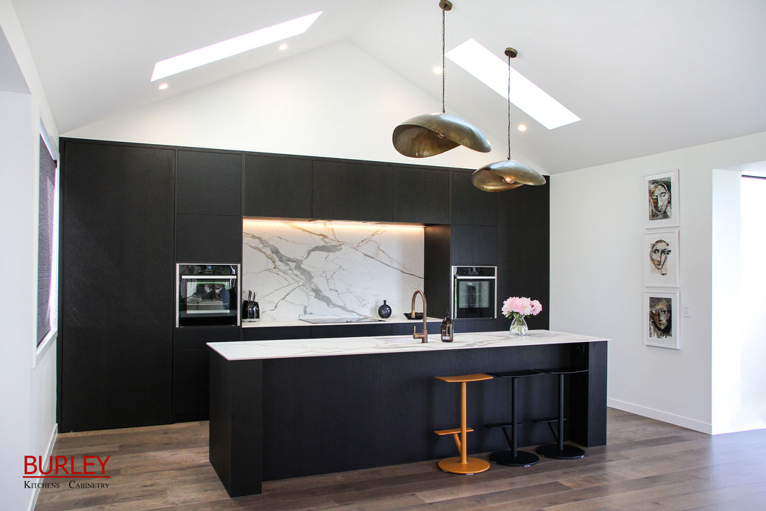 A black minimalist kitchen sits in a white room