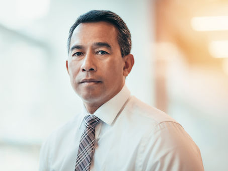 Portrait of a professional man wearing a white dress shirt and tie, looking confidently toward the camera in a softly lit office setting.