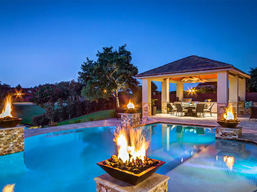 Completed swimming pool with raised water features and integrated fire bowls at dusk