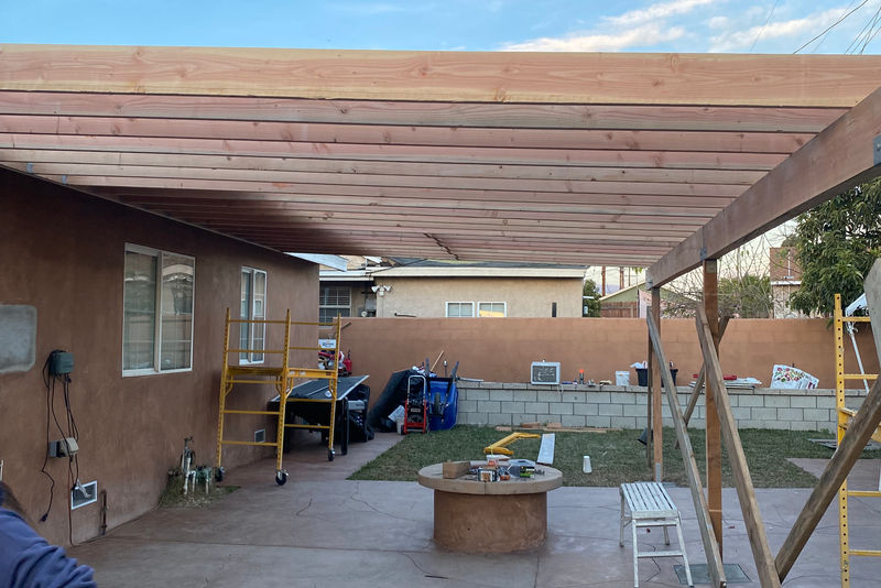 Wood patio cover framed with rafters and solid decking against an existing house wall