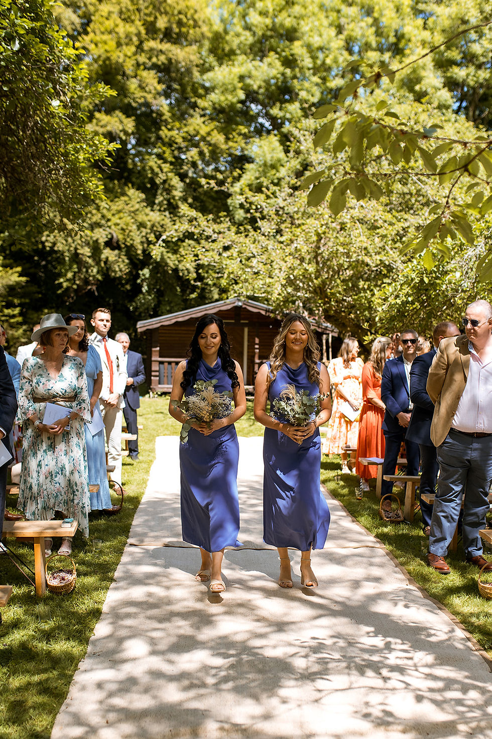 Brides maids in purple dresses walking down the aisle at outdoor garden wedding in the sunshine