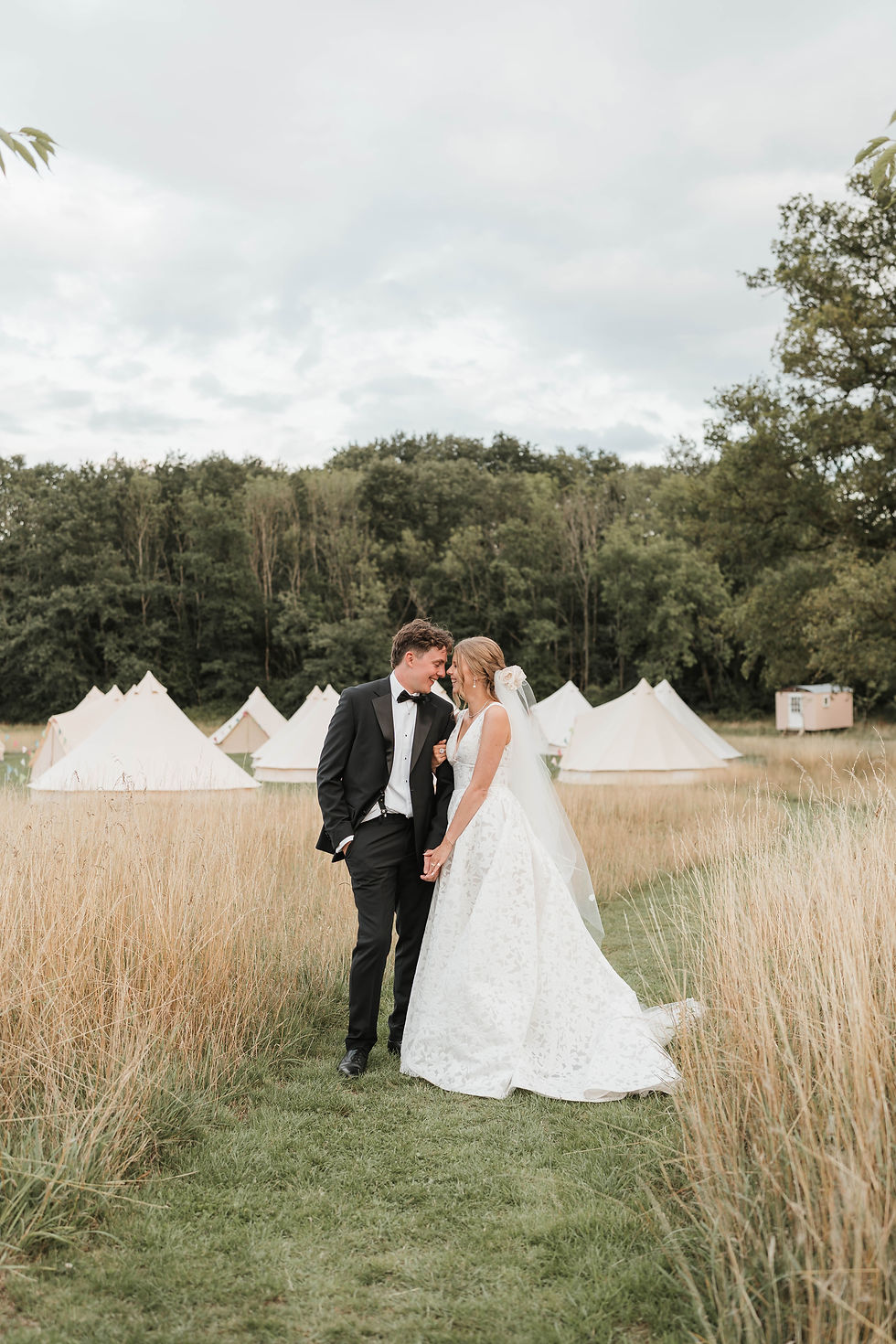 A bride and groom in a field, standing in front of bell tent wedding glamping in Godalming, Surrey