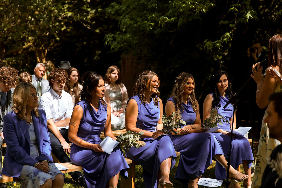 Bridesmaids sitting down at wedding ceremony in the garden with purple dresses and bouquets
