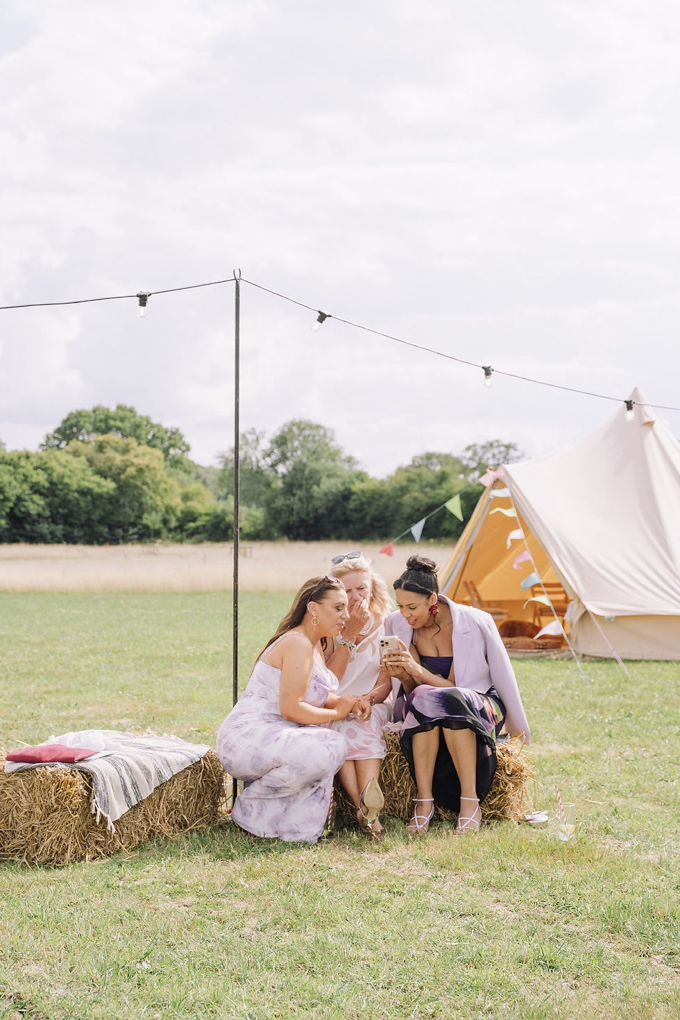 Wedding guests sitting on haybales at festival wedding with bell tents
