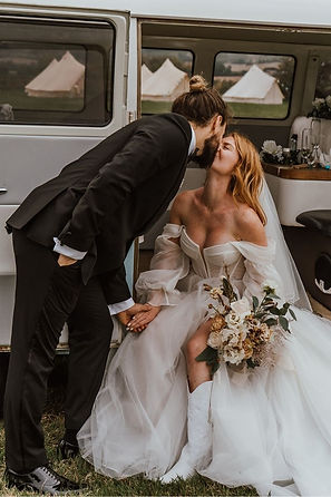 Bride and groom at festival wedding with bell tents in background in a vw campervan