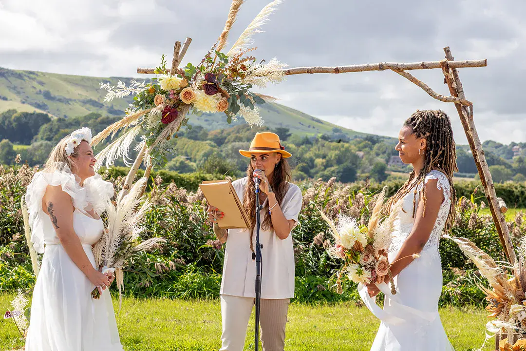 Bride and bride at outdoor wedding with rustic wedding arch and flowers