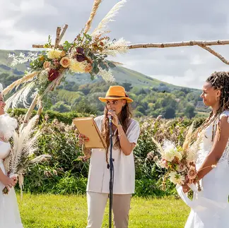 Bride and bride at outdoor wedding with rustic wedding arch and flowers