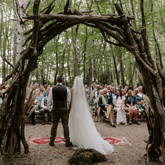 Woodland wedding ceremony with bride and groom and rustic weddnig arch