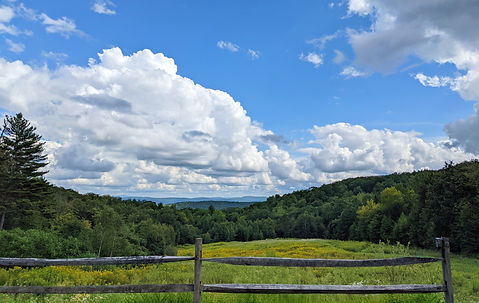 View of a old wood fence, field, and rolling green mountains.