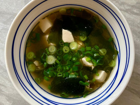 A home-cooked bowl of seaweed miso soup with soft tofu and a generous scatter of fresh spring onions, served in a white bowl with a blue rim — simple, nourishing and made with love.