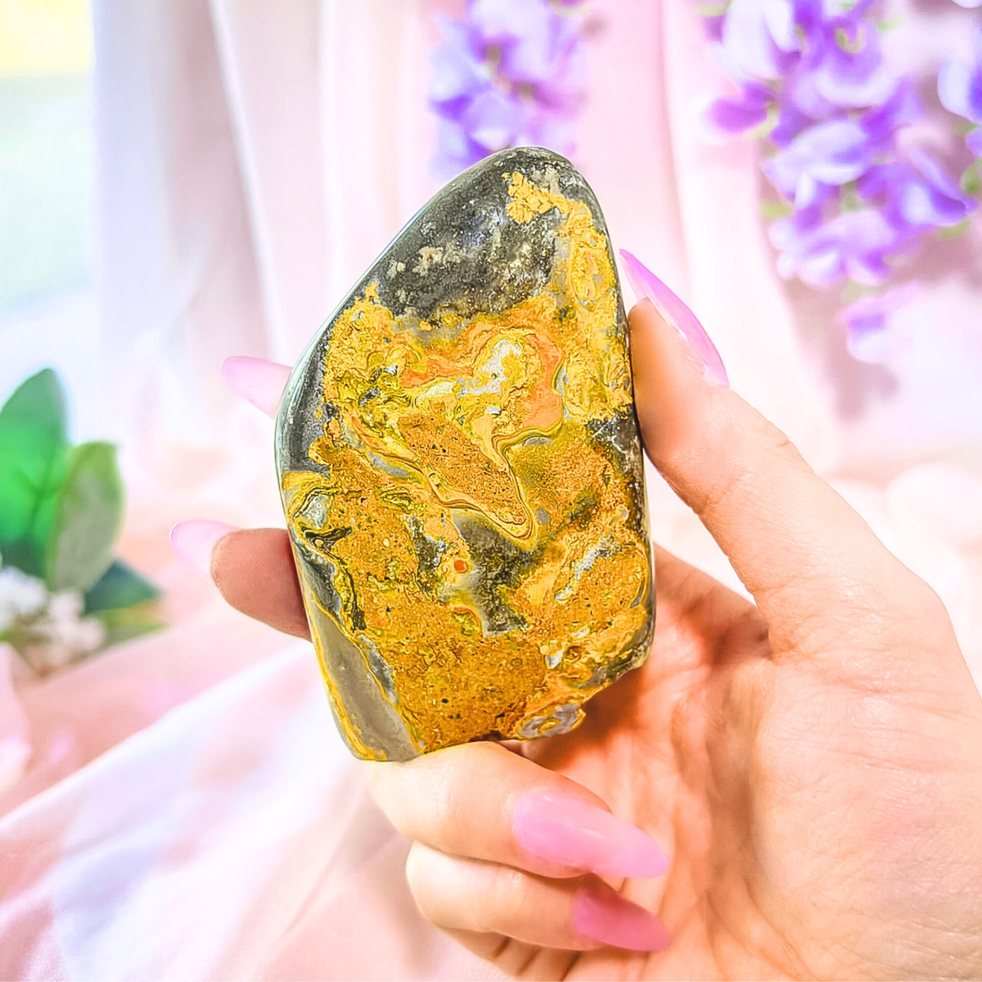 Hand holding the 3.2" Rare Indonesian Bumblebee Jasper – Polished Freeform Standing Stone against draped pink fabric.