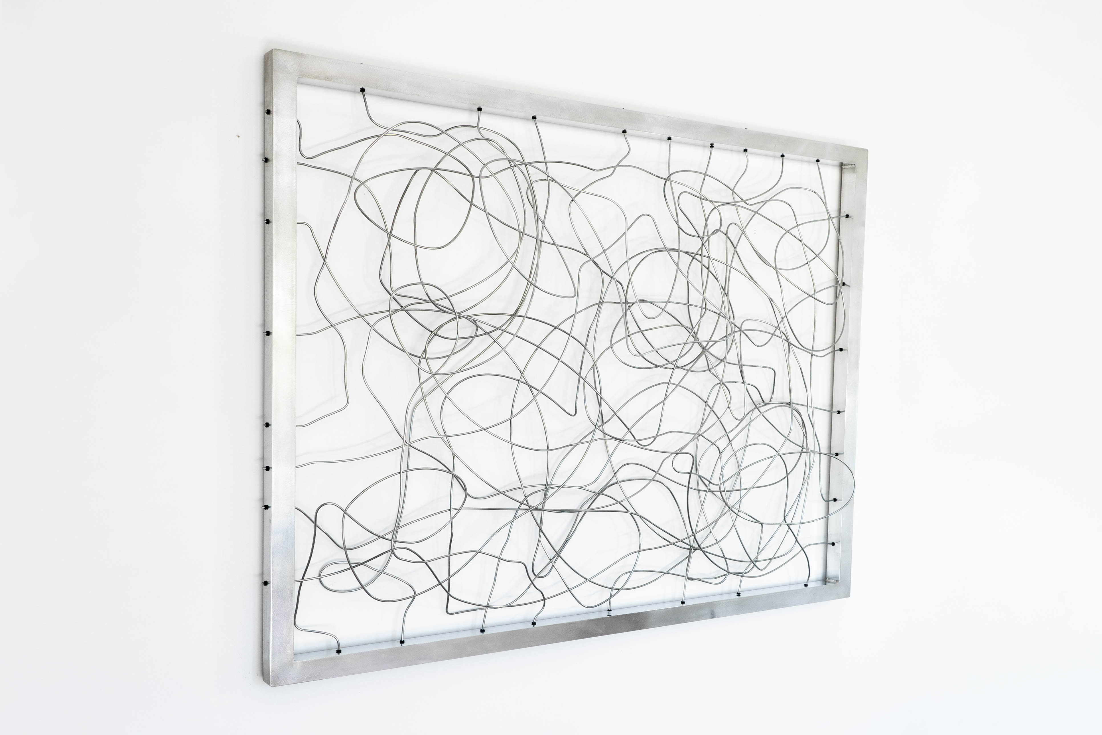 Stainless steel wire sculpture in rectangular frame by Cameron Hunt, mounted on a white wall.