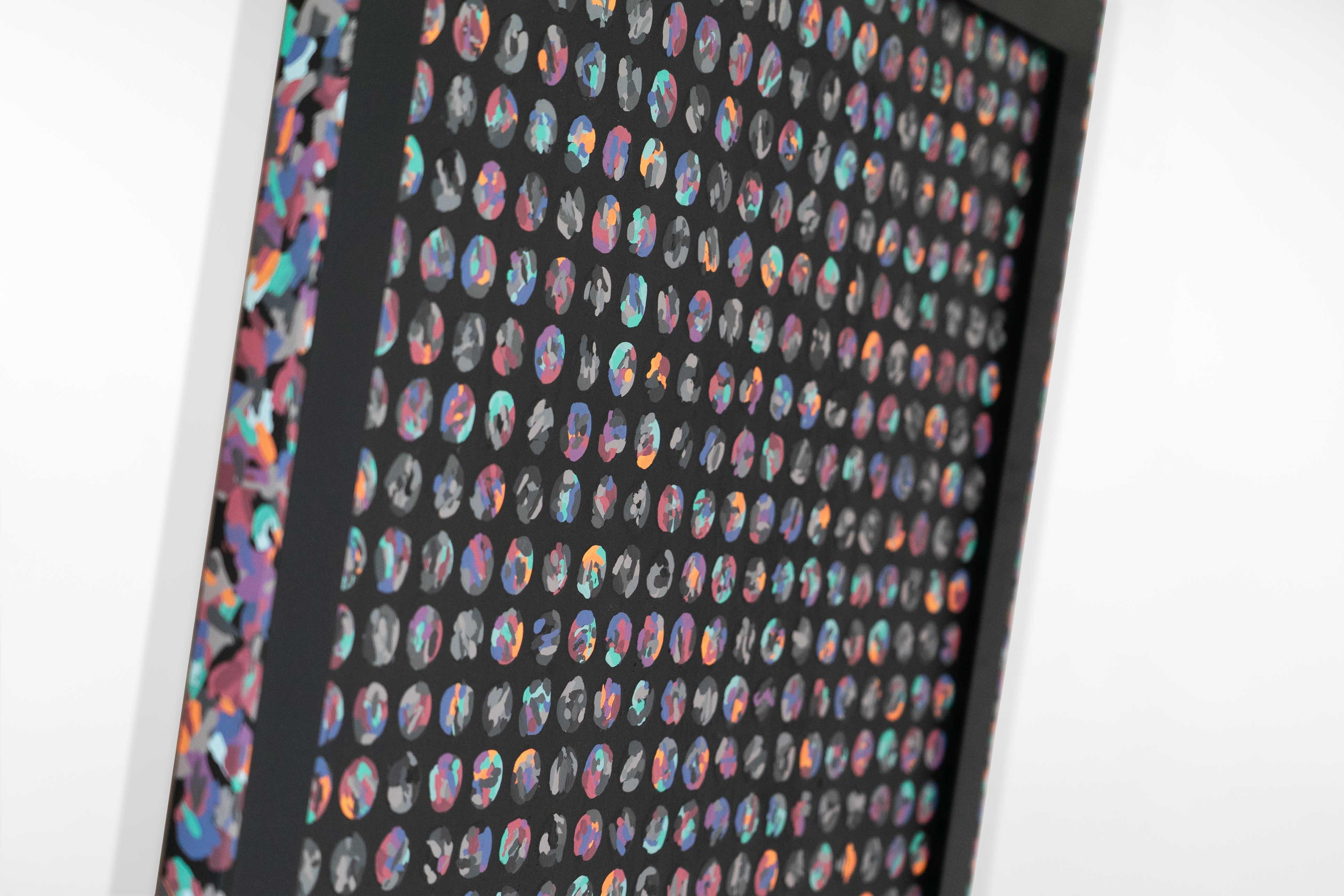Side view of a black-framed artwork by Cameron Hunt displaying hundreds of small, abstract circles in vibrant tones of purple, teal, orange, and grey, arranged in an orderly grid against a dark surface.