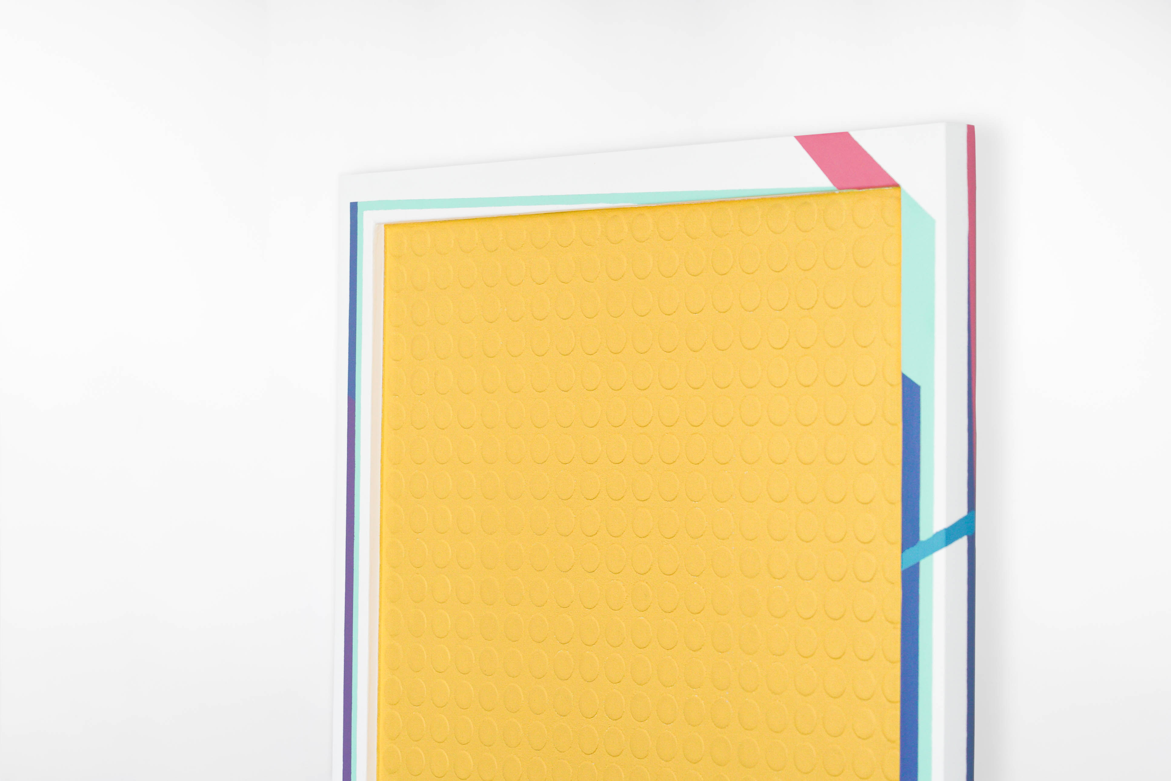 Close-up angled view of a contemporary painting by Cameron Hunt showcasing a raised yellow surface textured with a uniform grid of circular impressions. The border features crisp, geometric accents in teal, magenta, navy, and white.