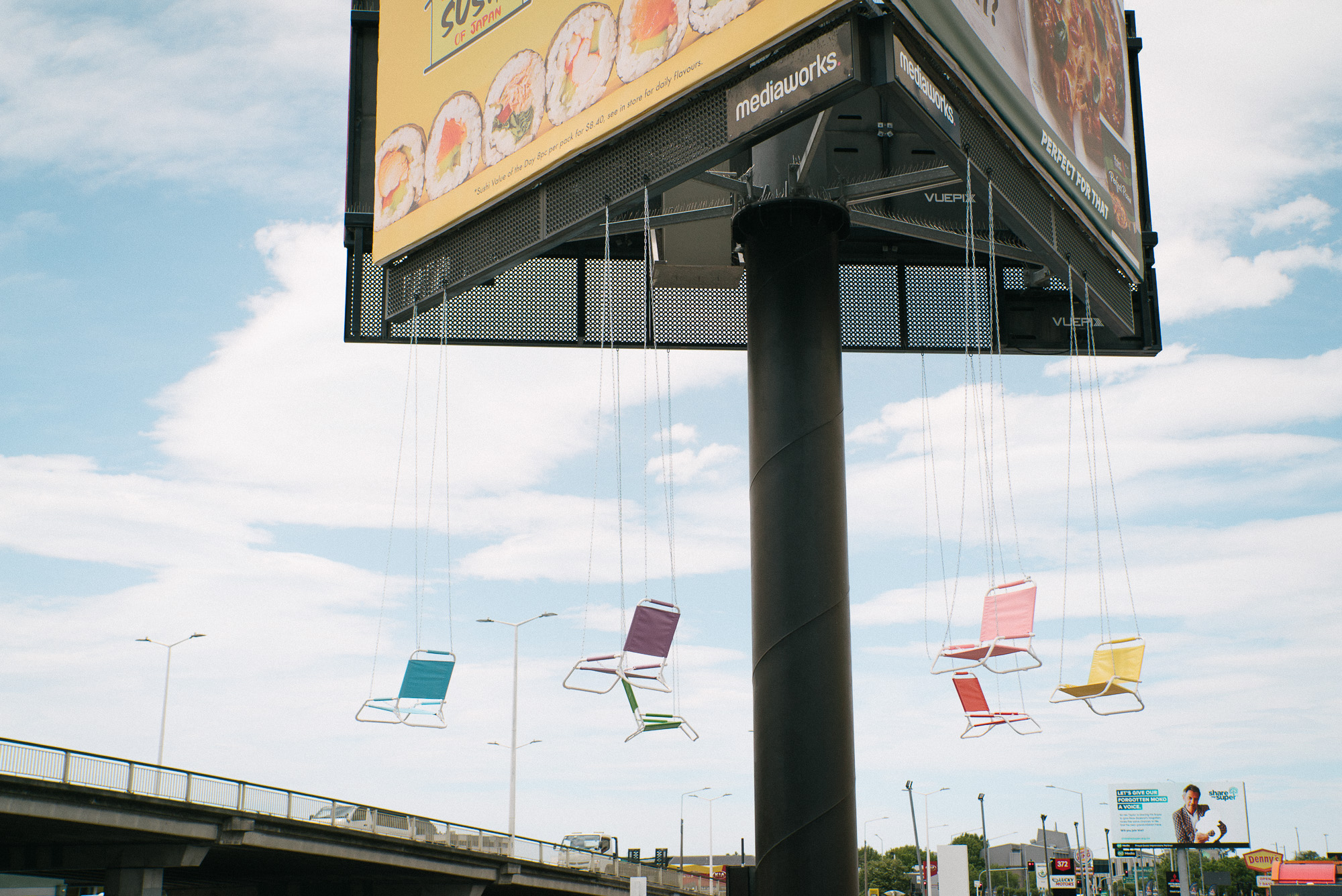 Street art installation resembling a swing ride featuring suspended chairs arranged like an amusement park ride in an urban environment.